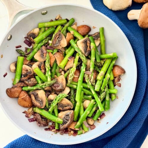 Grey frying pan with quartered cooked mushrooms and asparagus.